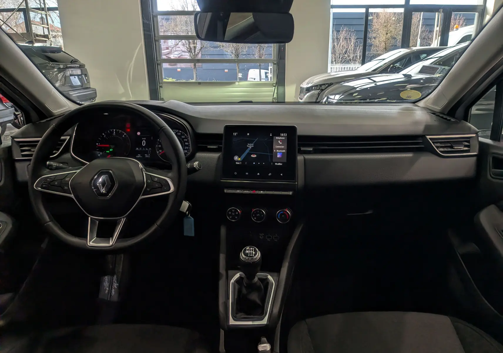 Vue intérieure frontale du tableau de bord de la Renault Clio V Business 2020 avec volant, écran tactile et levier de vitesses manuel.