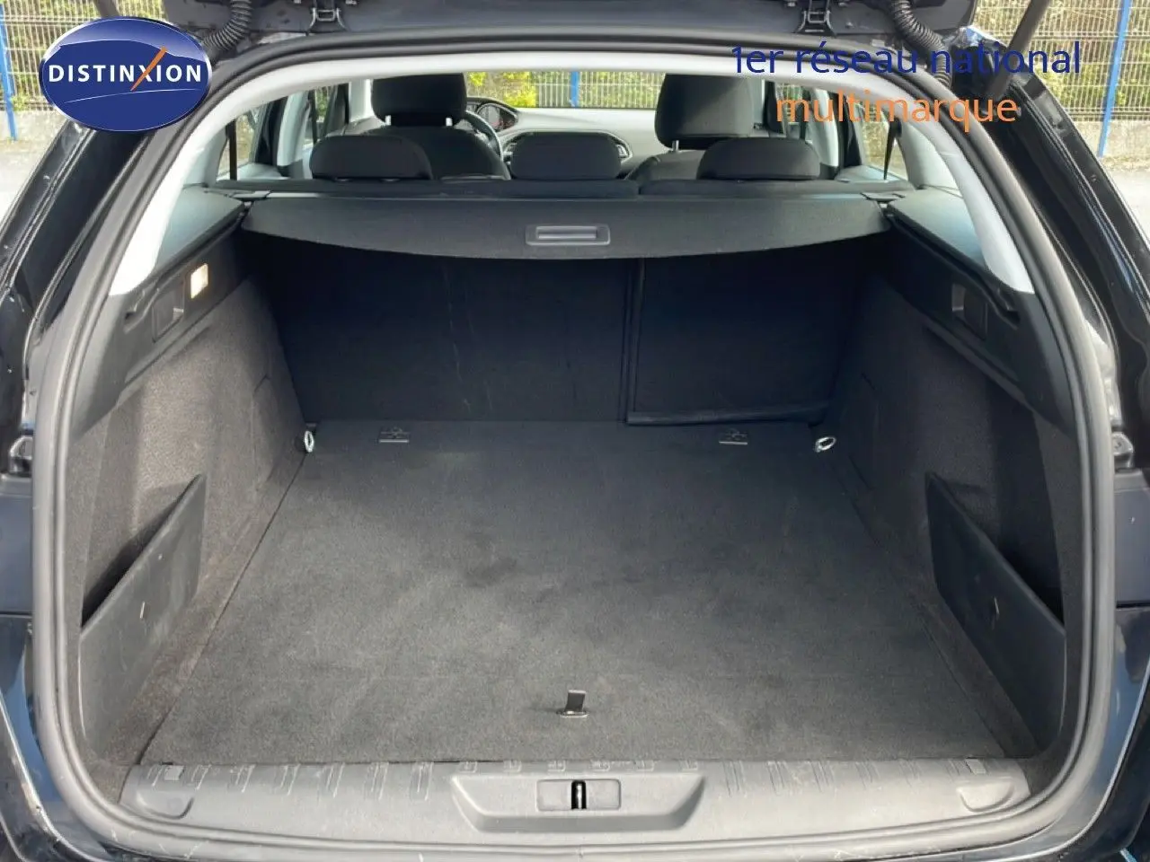 Coffre ouvert vu de l'arrière d'une Peugeot 308 SW noire, montrant un espace de chargement propre et spacieux.