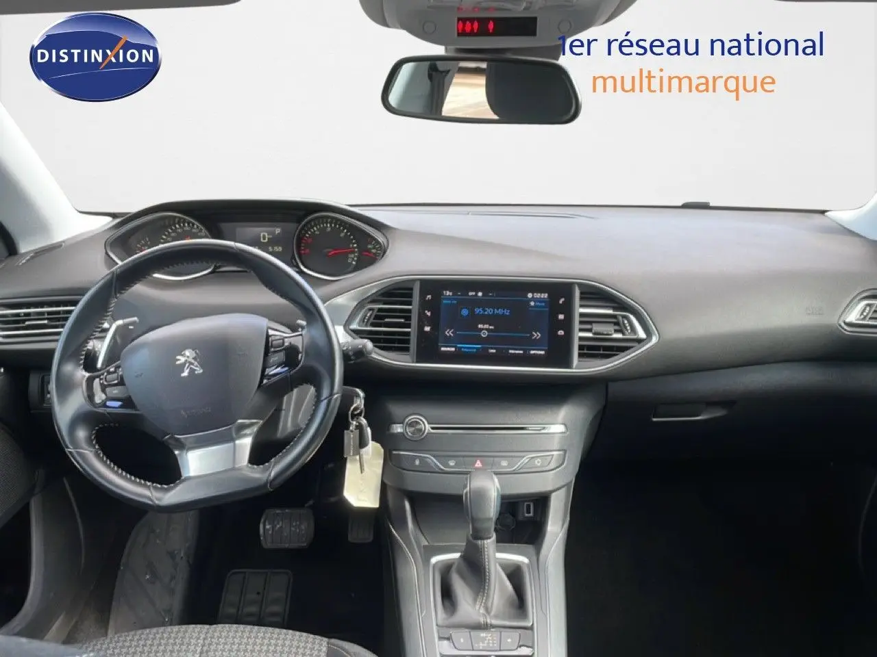 Vue intérieure frontale du tableau de bord noir de la Peugeot 308 SW 2019 avec volant cuir et écran tactile central allumé.