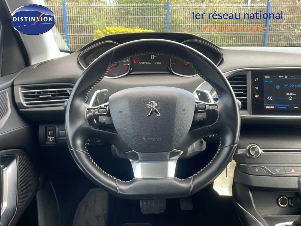 Vue intérieure centrée sur le volant cuir noir de la Peugeot 308 SW 2019 avec tableau de bord et écran multimédia.