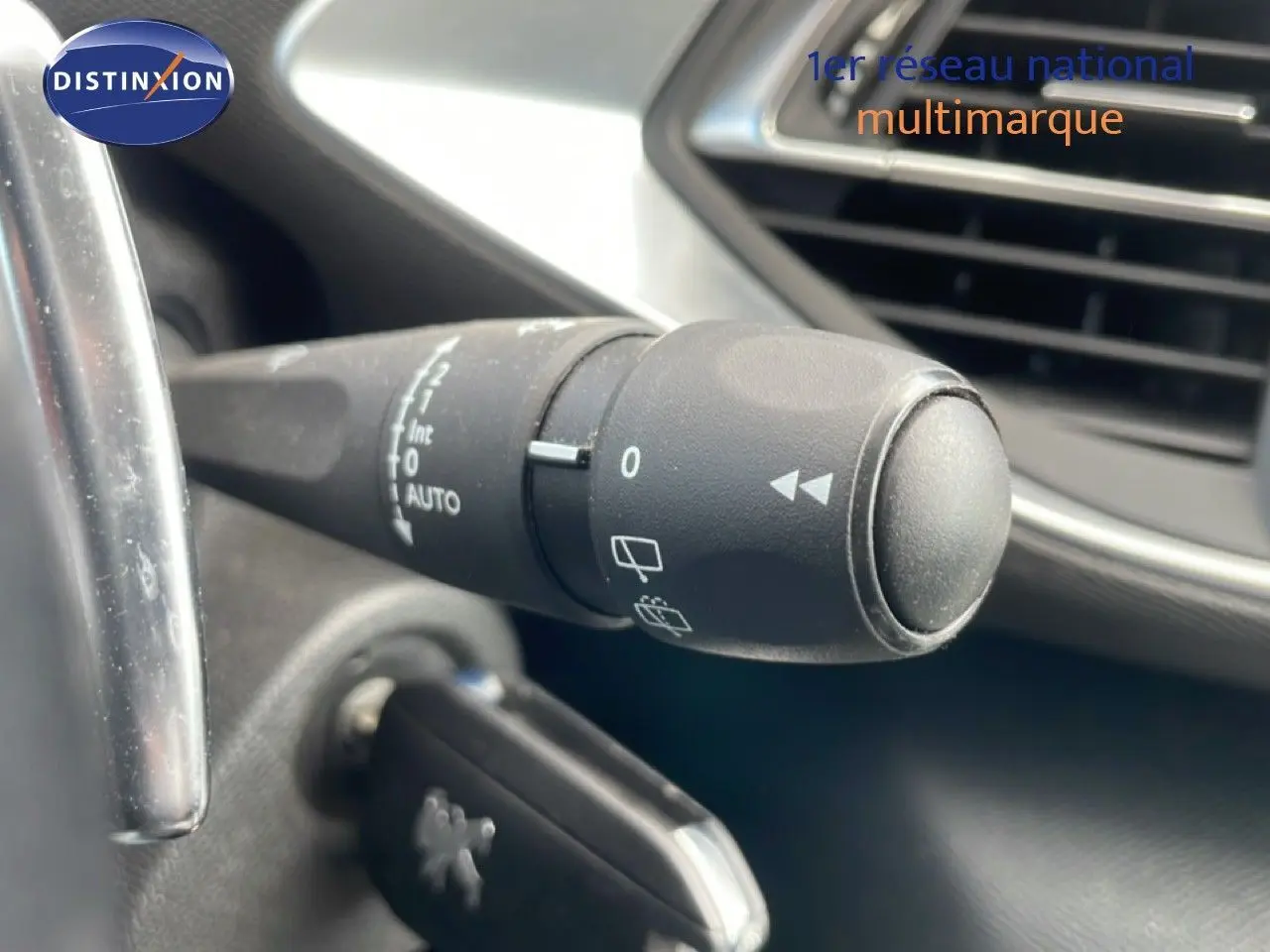 Gros plan sur la commande d’essuie-glace à gauche du volant dans l’habitacle noir d’une Peugeot 308 SW 2019.