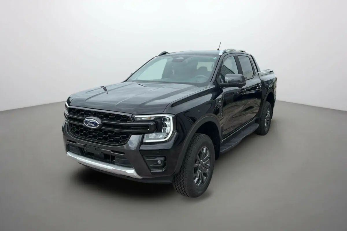 Ford Ranger 3.0 V6 Wildtrak Plus noir agate vu en 3/4 avant droit, avec jantes alu et barres de toit visibles.