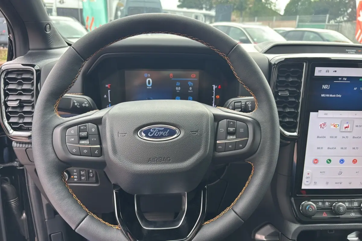 Vue rapprochée du volant cuir noir avec surpiqûres marron du Ford Ranger 2025, tableau de bord et écran tactile visibles.
