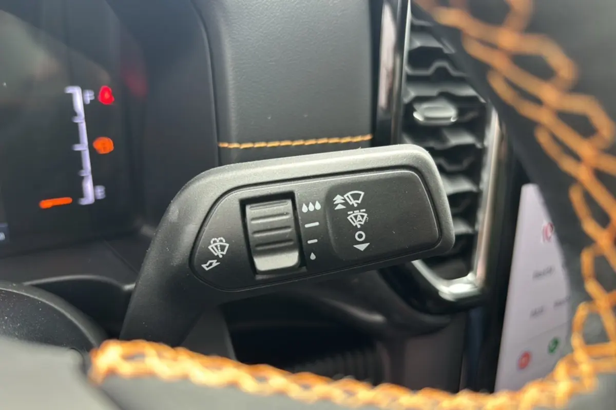 Gros plan sur la manette d’essuie-glace du Ford Ranger Wildtrak Plus noir avec surpiqûres orange du volant en cuir.