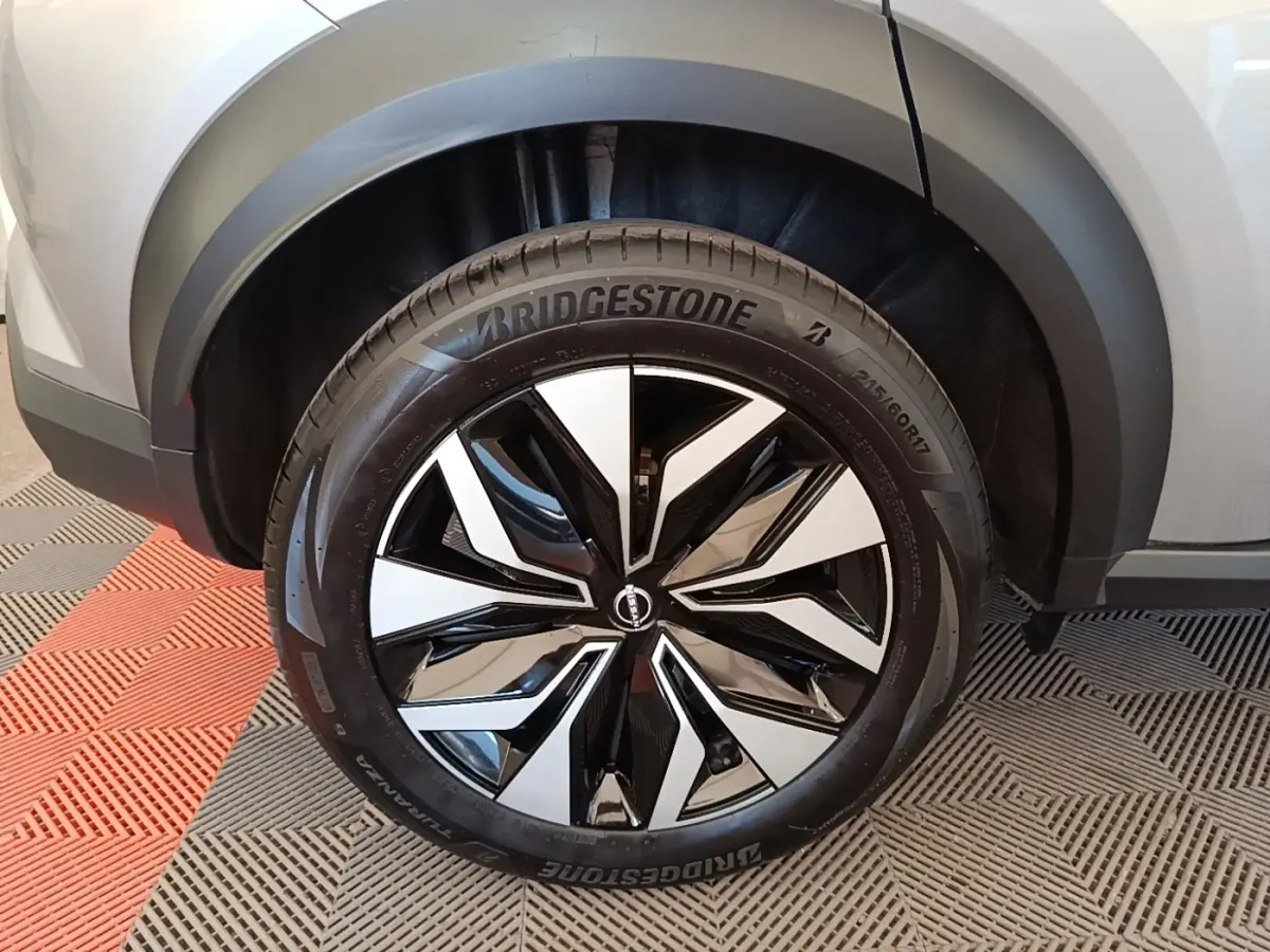Gros plan sur la roue avant droite du Nissan Juke gris clair, jante alliage noir et argentée au design moderne.