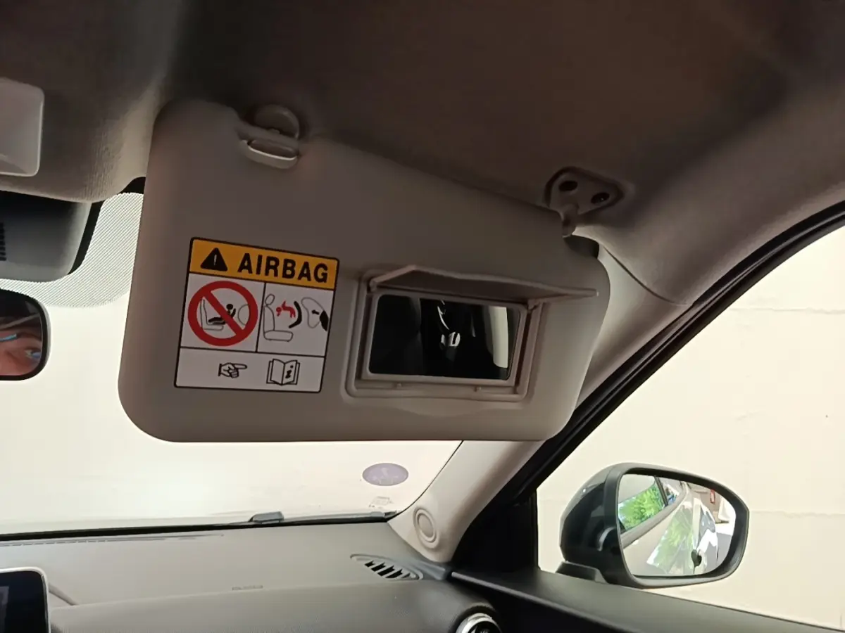 Vue intérieure côté passager du pare-soleil gris clair avec miroir et avertissement airbag du Nissan Juke 2023.