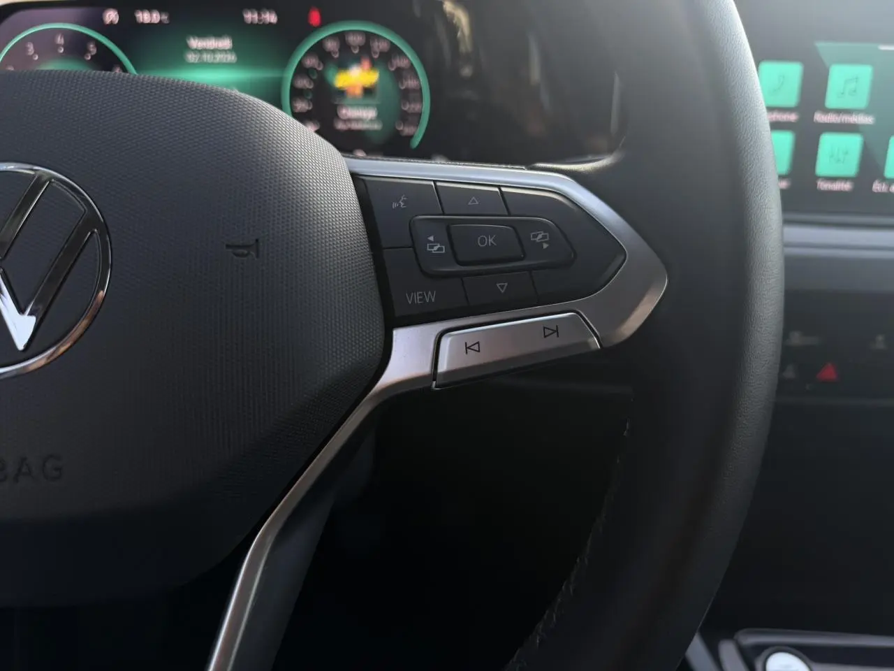 Gros plan sur le volant multifonction noir de la Volkswagen Golf VIII 2024, avec commandes intégrées et tableau de bord digital en arrière-plan.