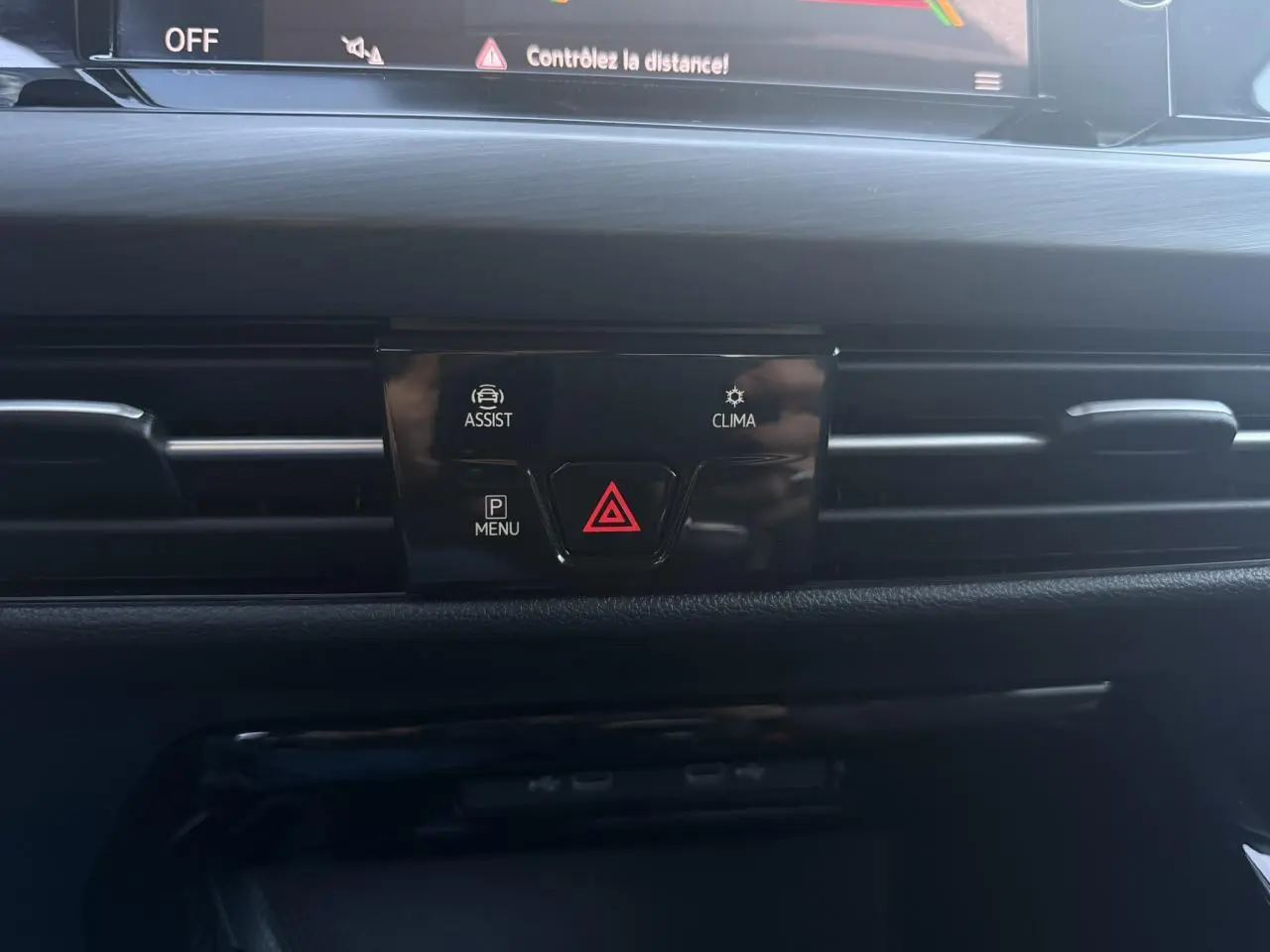 Gros plan sur la console centrale noire de la Volkswagen Golf VIII 2024, avec boutons d'assistance et climatisation visibles.
