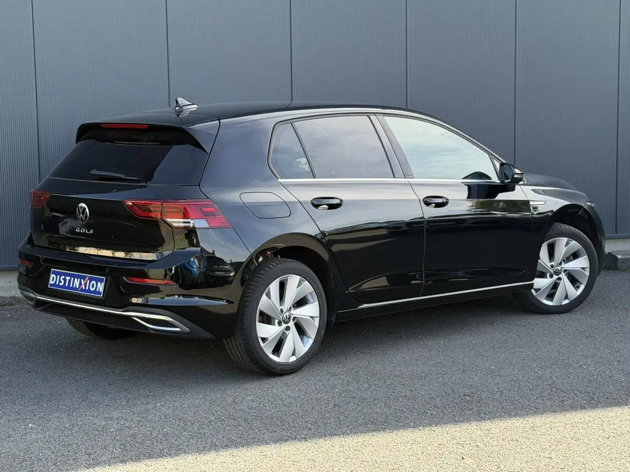 Vue 3/4 arrière droite d'une Volkswagen Golf VIII noire avec jantes alliage 17 pouces et baguettes chromées.