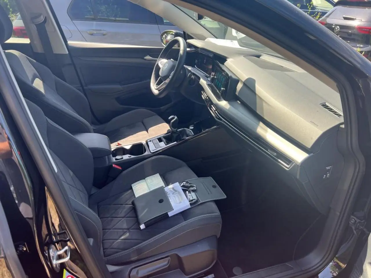 Vue intérieure côté conducteur de la Volkswagen Golf VIII noire, montrant sièges en microfleece et tableau de bord moderne.