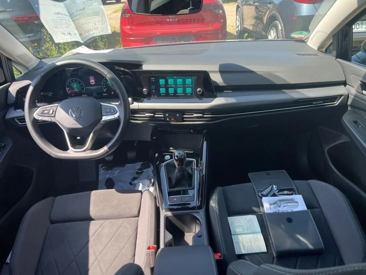 Vue intérieure avant de la Volkswagen Golf VIII noire, montrant le volant cuir multifonction et la boîte manuelle.
