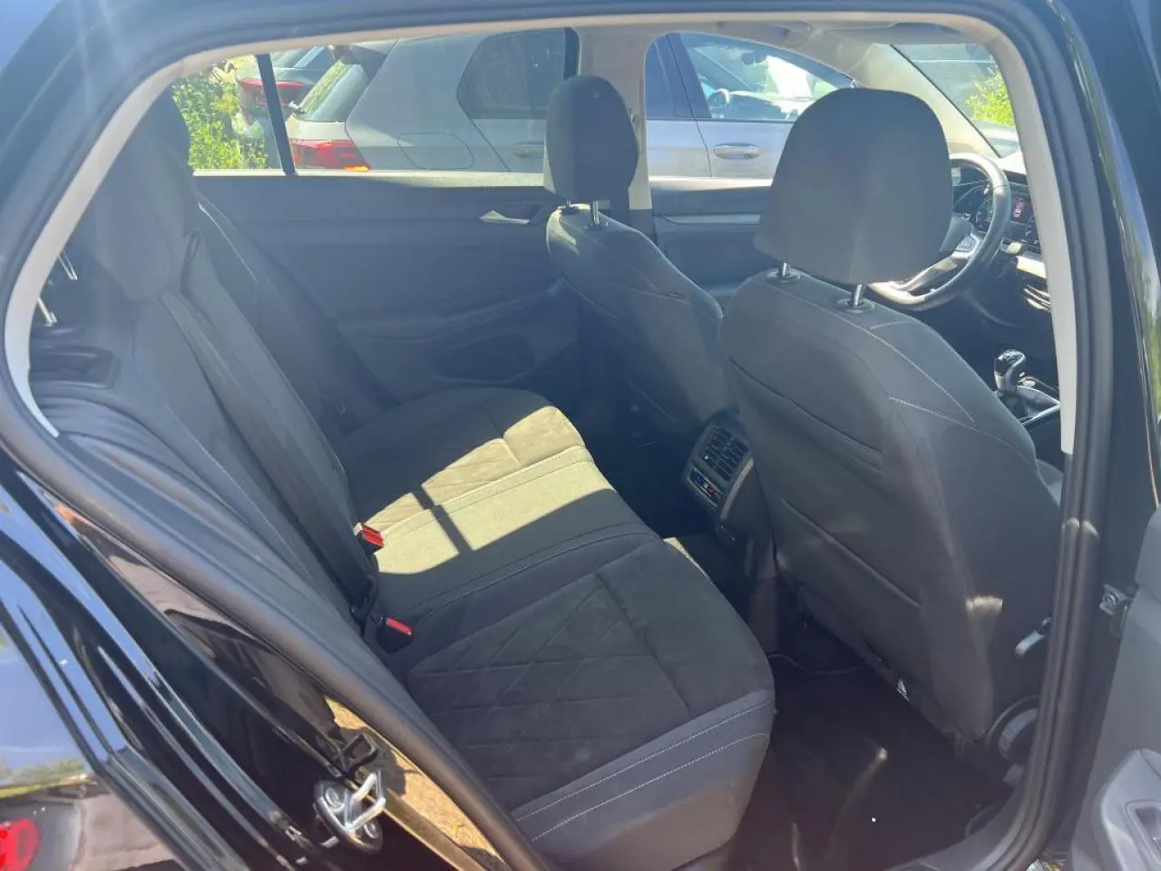 Vue intérieure arrière côté gauche de la Volkswagen Golf VIII noire, montrant les sièges arrière et avant en sellerie Microfleece.