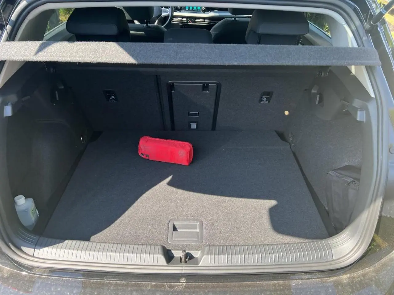 Vue du coffre ouvert d’une Volkswagen Golf VIII 1.5 TSI noire, montrant un espace de rangement avec trousse de secours rouge.
