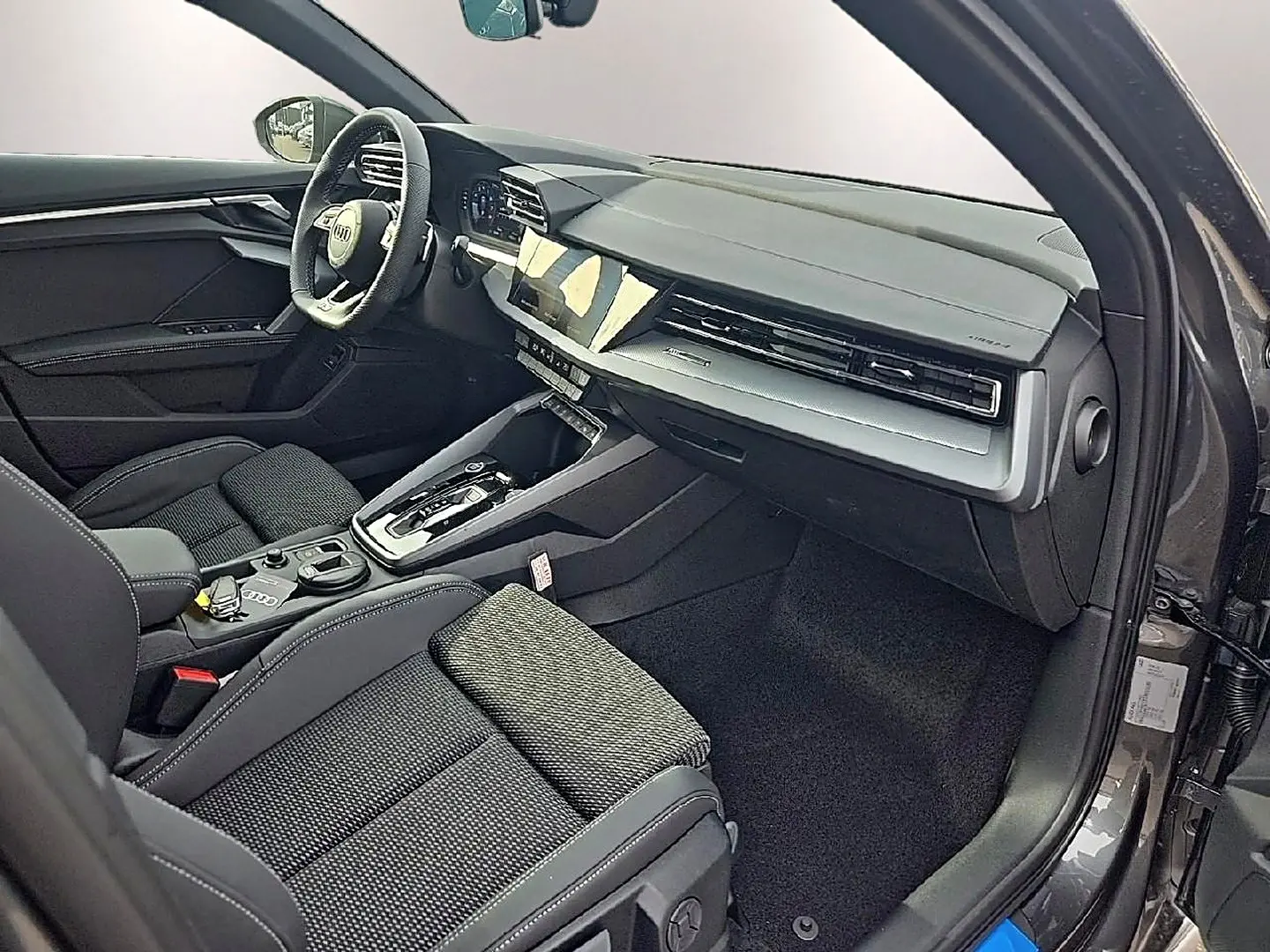 Vue intérieure côté passager avant d'une Audi A3 Sportback 2026 avec sellerie noire et tableau de bord moderne gris.