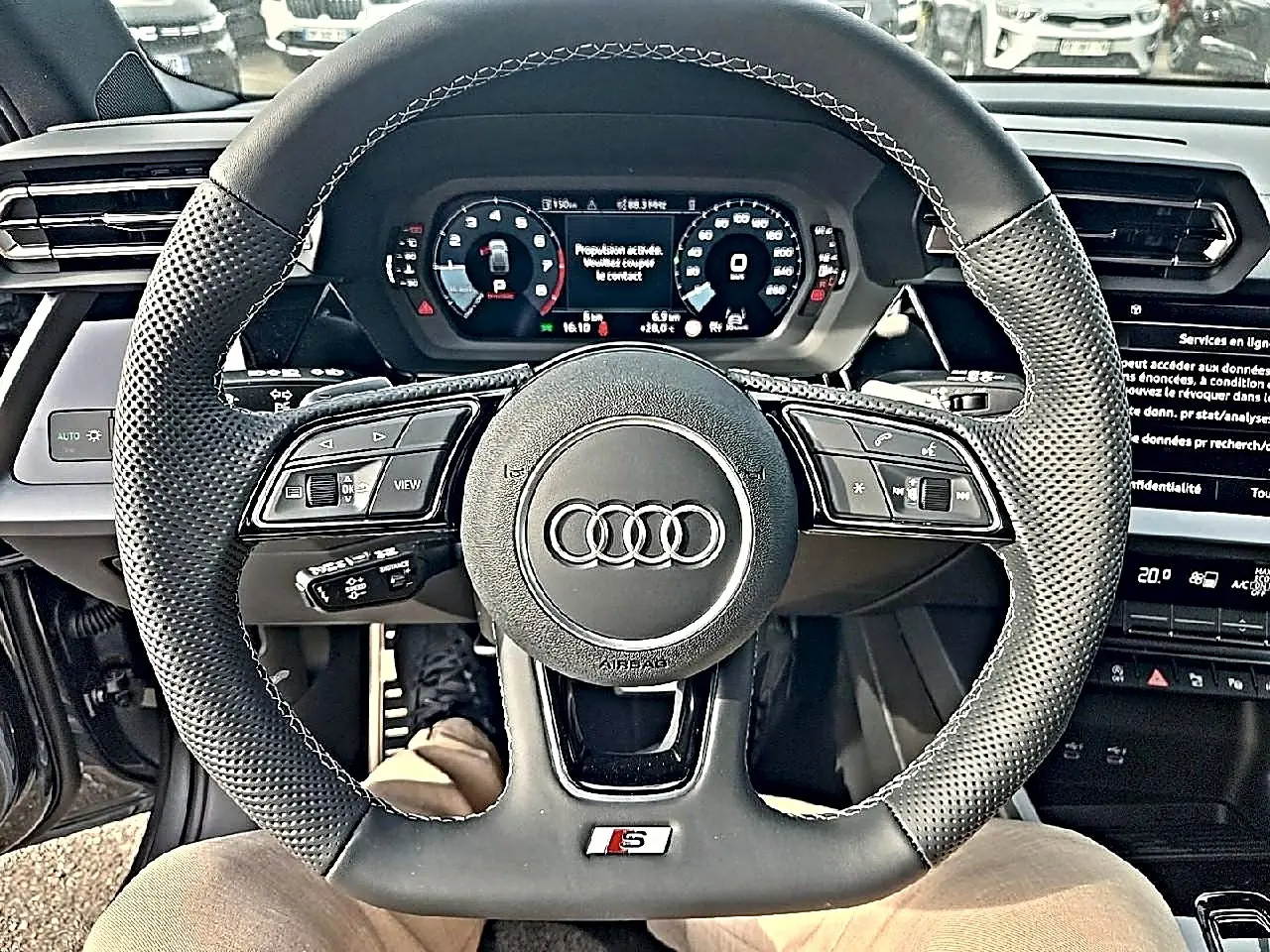 Vue rapprochée du volant sport en cuir noir avec logo Audi et tableau de bord numérique d’une Audi A3 Sportback.