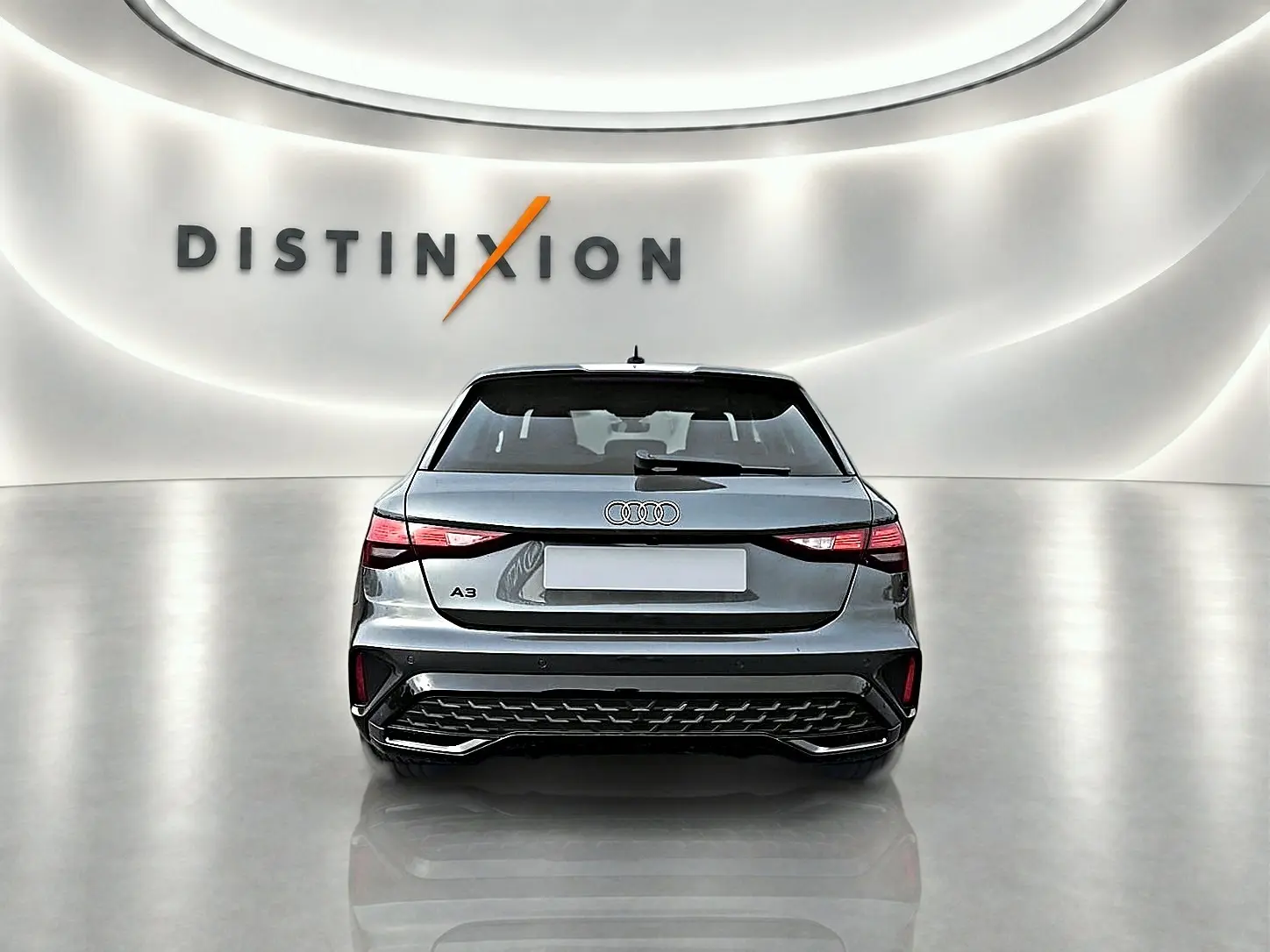 Vue arrière d'une Audi A3 Sportback gris Daytona avec feux LED et diffuseur arrière noir dans un showroom lumineux.