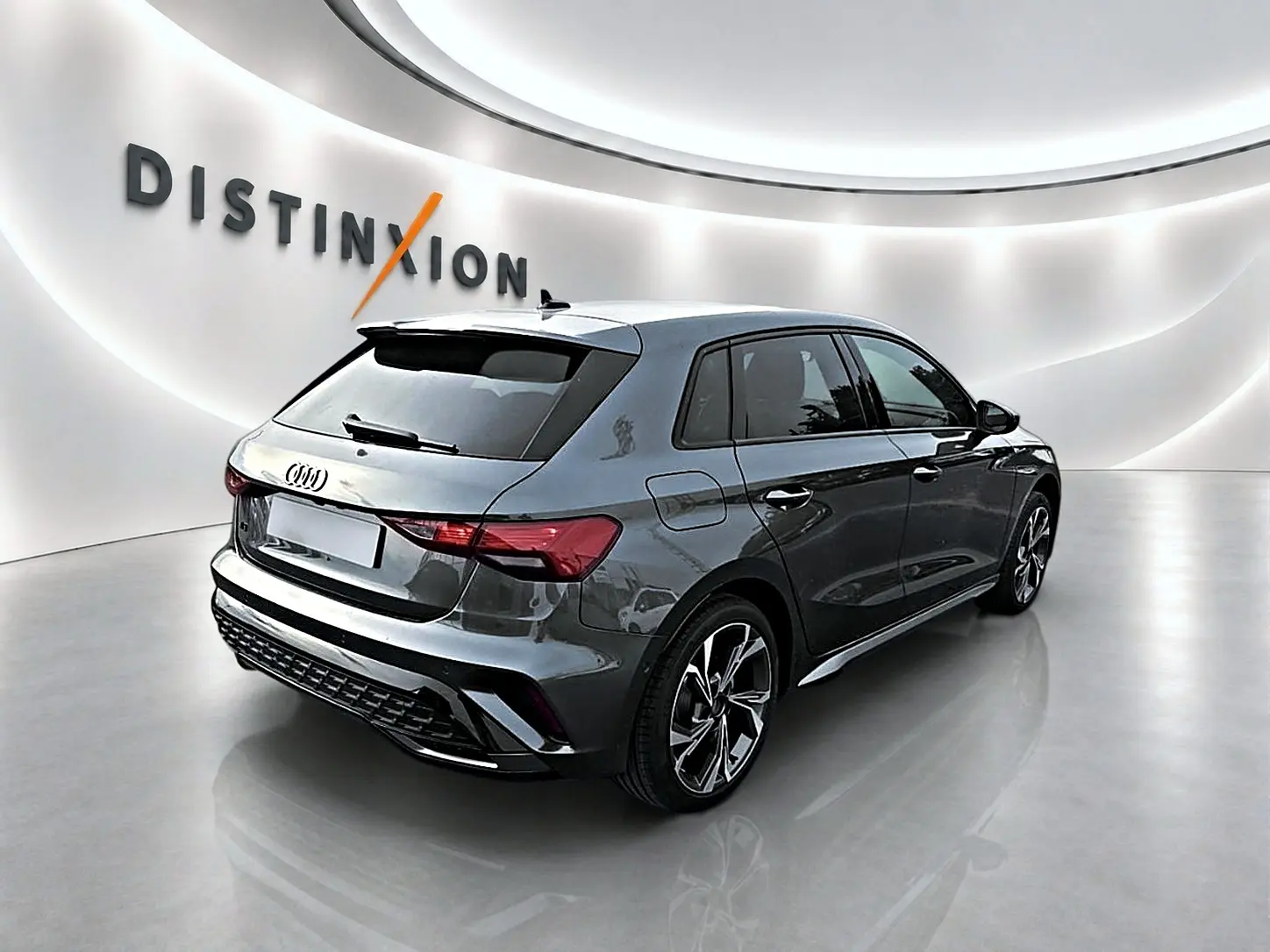 Audi A3 Sportback gris Daytona vue 3/4 arrière droit dans un showroom lumineux avec jantes alu distinctives.
