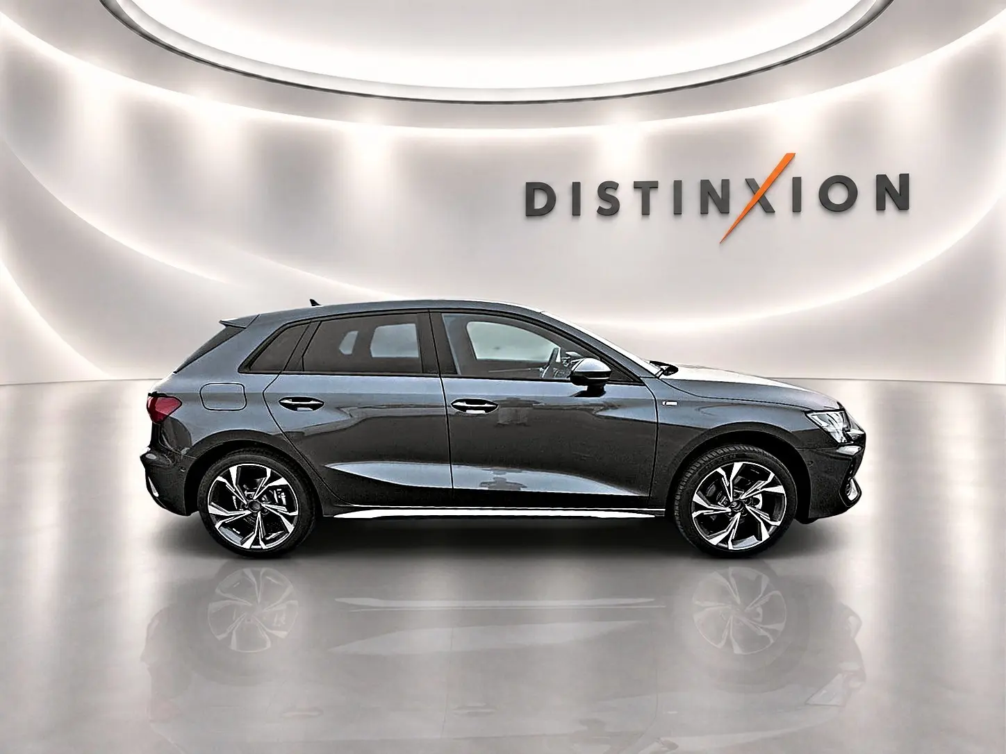 Audi A3 Sportback gris Daytona vue de profil côté gauche dans un showroom lumineux avec logo Distinxion en arrière-plan.