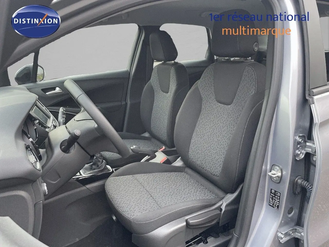 Vue intérieure côté conducteur de l'Opel Crossland gris minéral métal, montrant les sièges en tissu gris et la console centrale.