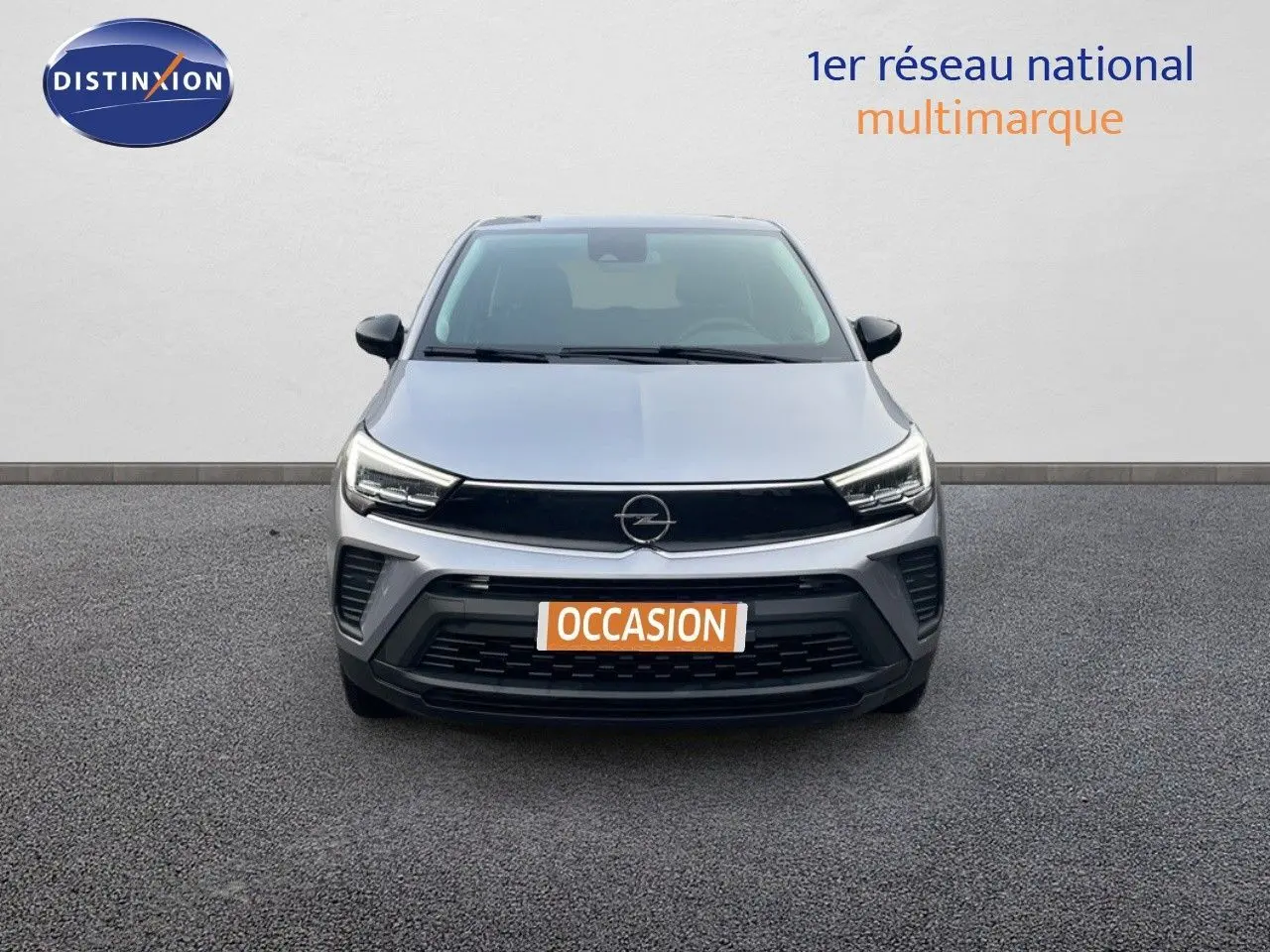 Vue frontale d'un Opel Crossland gris minéral métal avec calandre noire et phares LED allumés sur fond neutre.