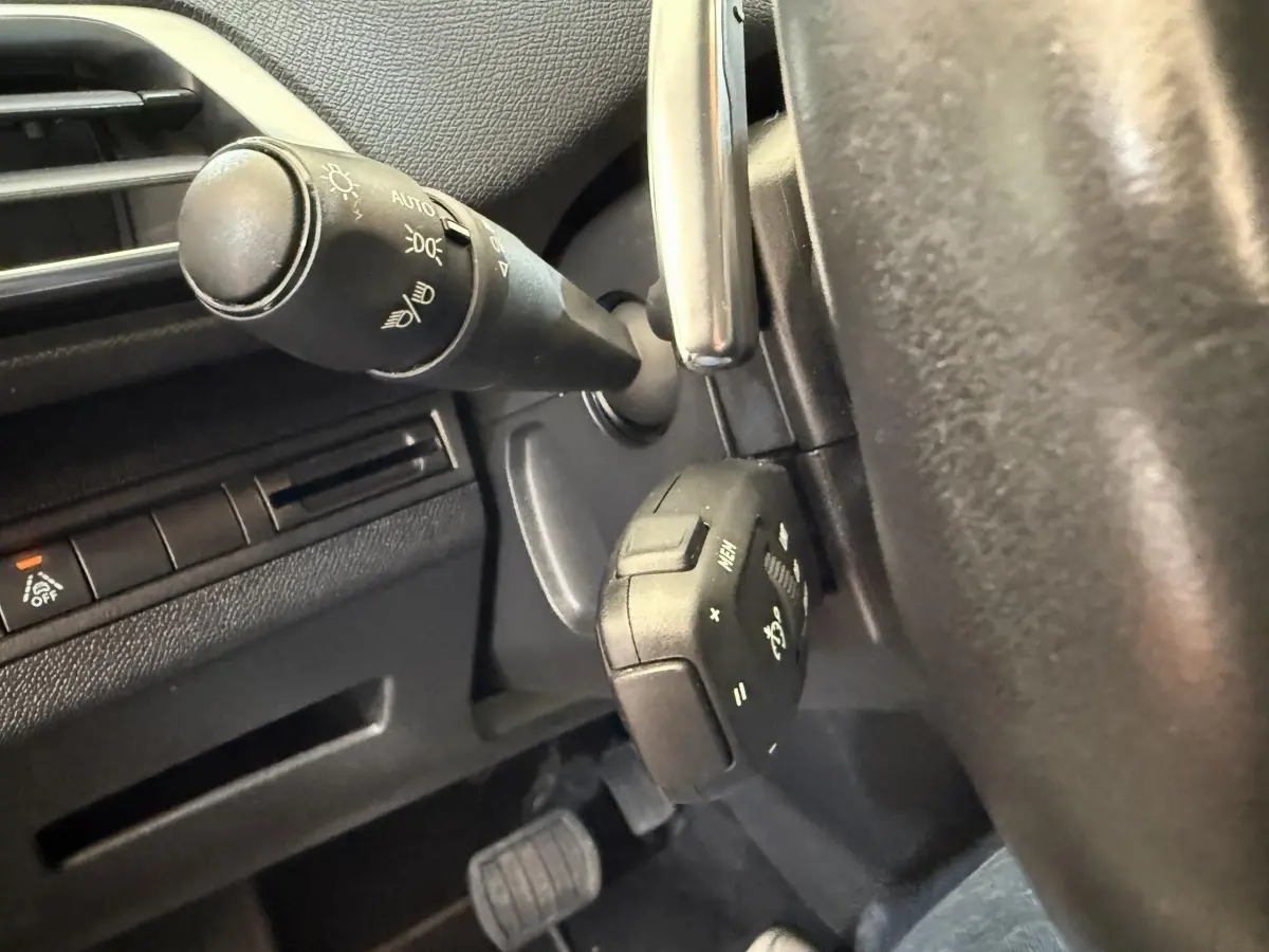 Gros plan sur la commande multifonction noire au volant d’un Peugeot 3008 bleu, avec tableau de bord partiel visible.