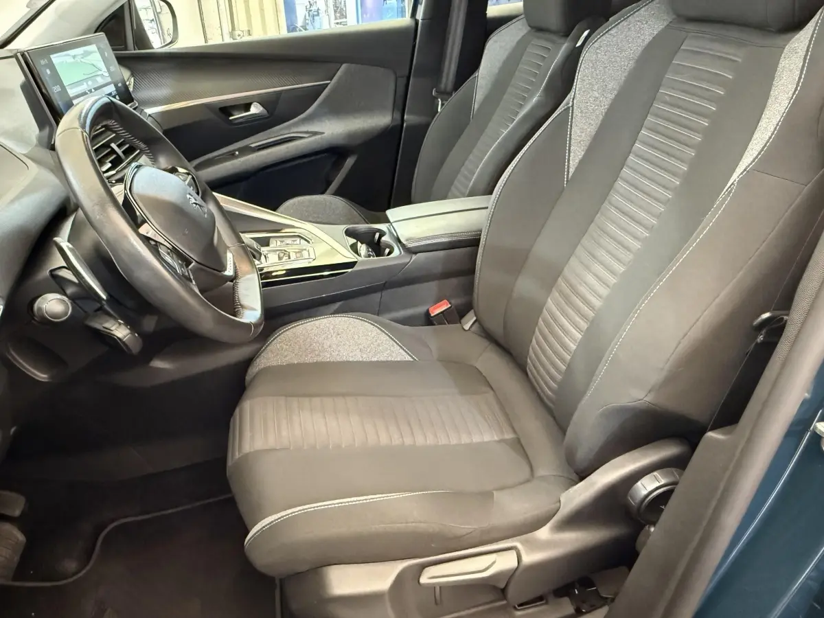 Vue intérieure côté conducteur du Peugeot 3008 bleu, montrant le volant cuir, sièges tissu bicolores et console centrale moderne.