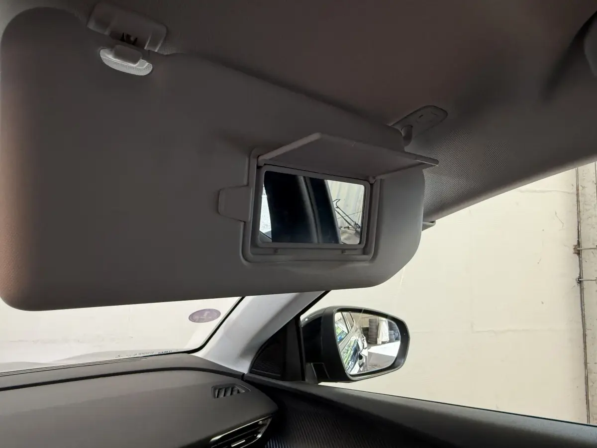 Détail intérieur du pare-soleil côté conducteur avec miroir, rétroviseur extérieur droit et tableau de bord noir du Peugeot 3008 bleu.