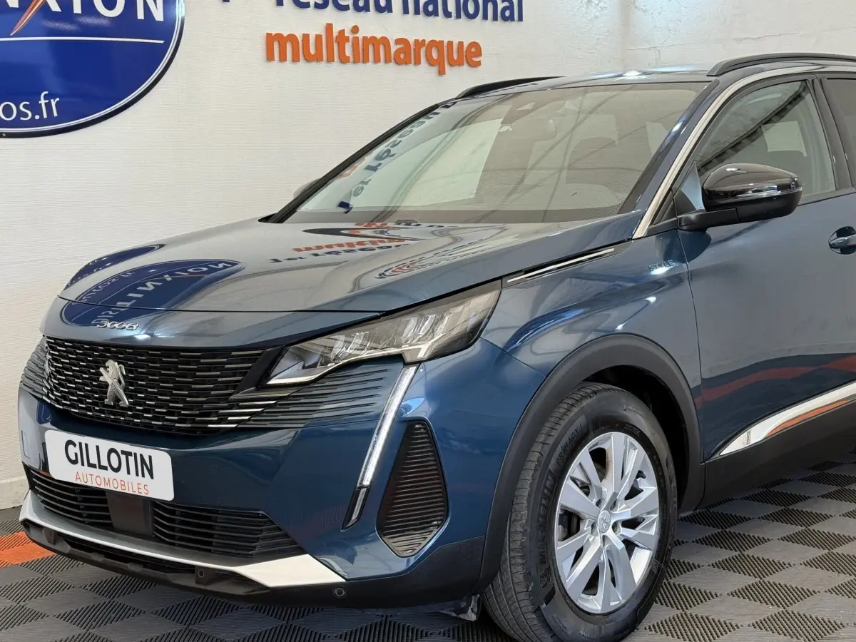 Vue 3/4 avant droit d'un Peugeot 3008 bleu avec calandre noire et feux LED distinctifs, stationné en intérieur.