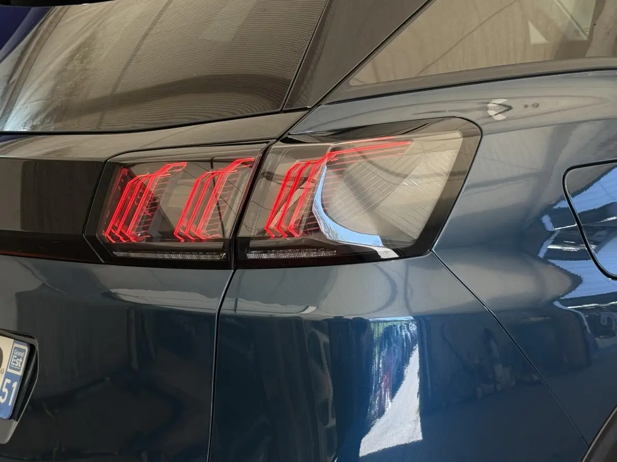 Gros plan sur le feu arrière droit rouge d’un Peugeot 3008 bleu, soulignant la ligne noire entre les feux.