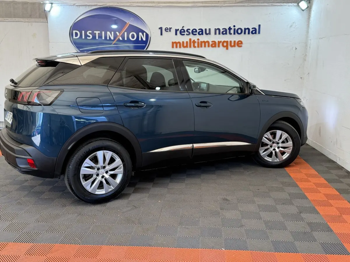 Vue latérale droite d’un Peugeot 3008 bleu 2021 avec jantes alliage et rails de toit assortis en intérieur showroom.