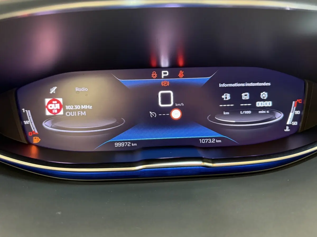 Affichage numérique du tableau de bord du Peugeot 3008 bleu, montrant la radio, vitesse à 0 km/h et jauges carburant et température.