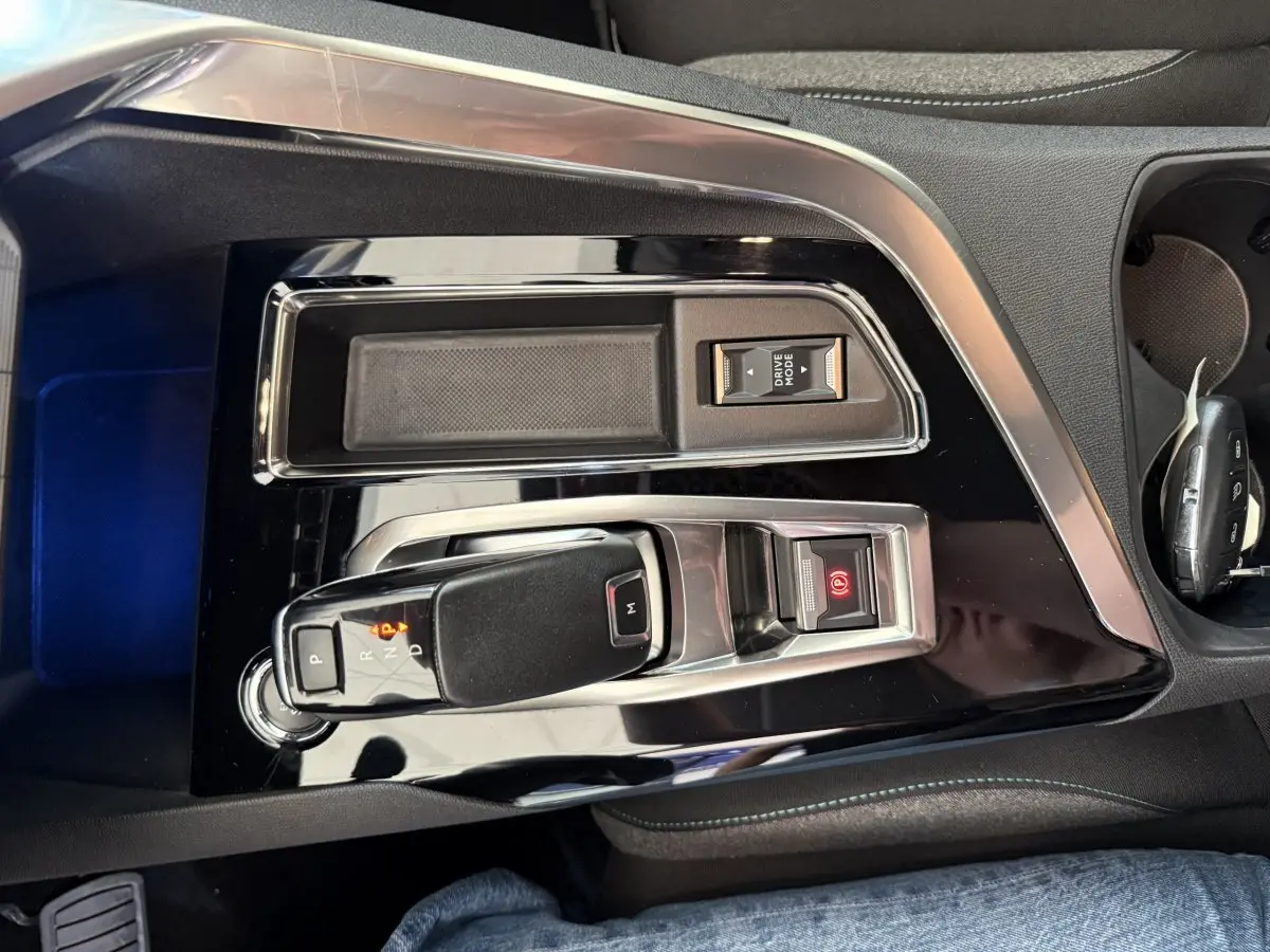 Gros plan sur la console centrale noire brillante du Peugeot 3008 bleu, avec levier de vitesse automatique et bouton frein à main électrique.