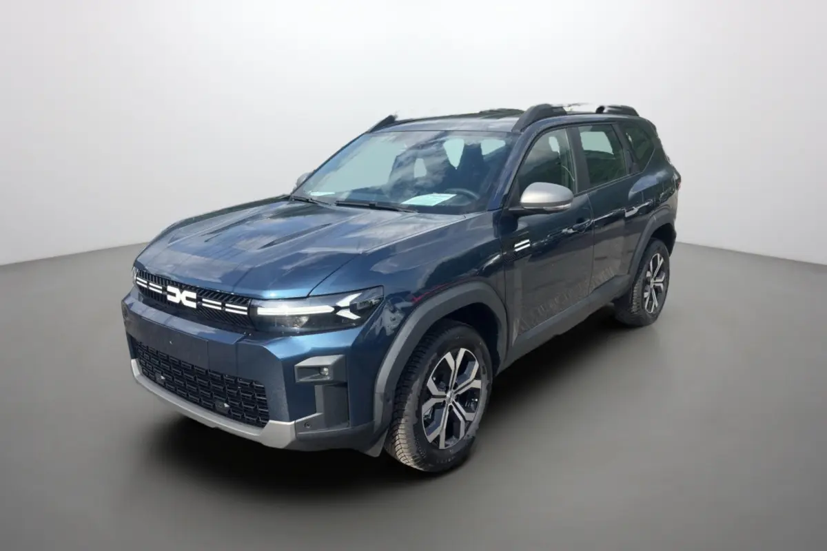 SUV Dacia Bigster bleu indigo en 3/4 avant droit, avec barres de toit et jantes alu 17 pouces visibles.
