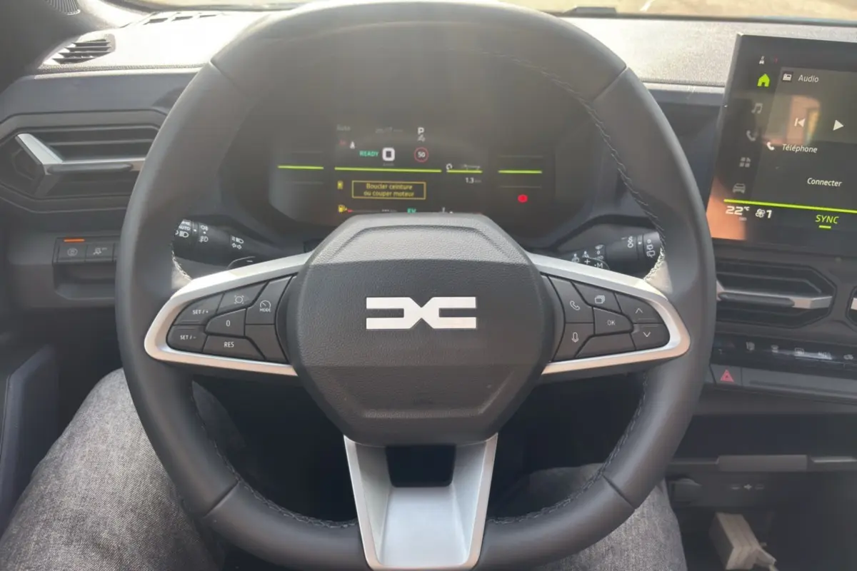 Vue intérieure centrée sur le volant cuir du Dacia Bigster Hybrid-G 150 avec tableau de bord numérique et écran tactile.