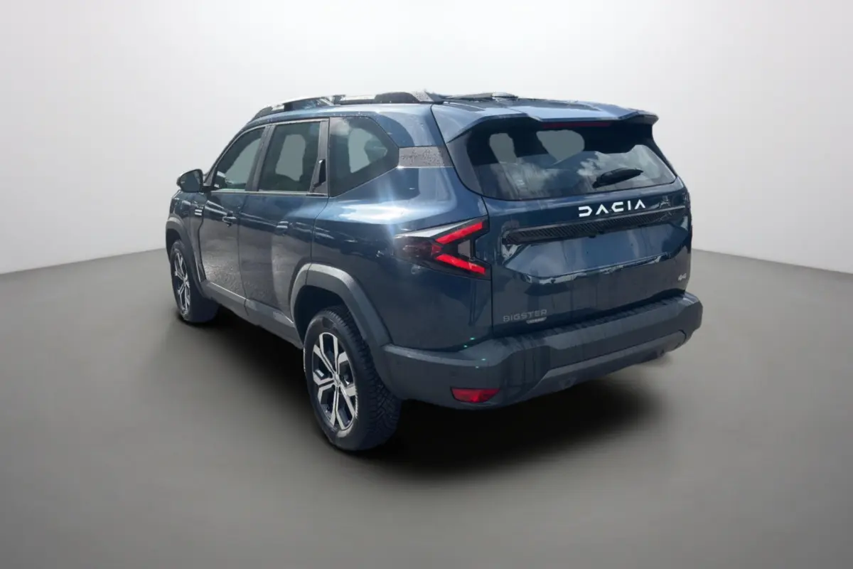 Vue 3/4 arrière droite d'un Dacia Bigster bleu indigo avec barres de toit et jantes alu 17 pouces.