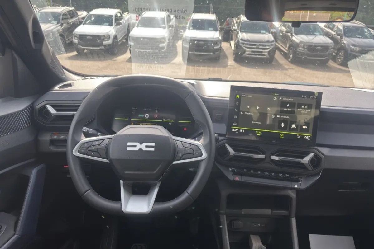 Vue intérieure du tableau de bord du Dacia Bigster Hybrid-G 150, avec volant cuir et écran tactile central allumé.