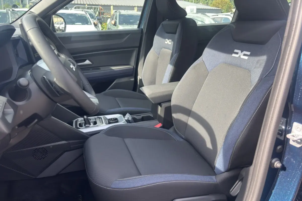 Vue intérieure côté conducteur du Dacia Bigster bleu indigo, mettant en valeur les sièges tissu bicolores avec logo brodé.