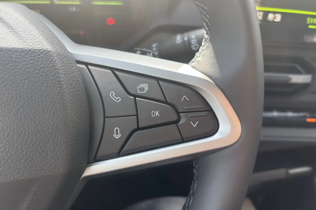 Gros plan sur les commandes au volant cuir du Dacia Bigster Hybrid-G 150, intérieur noir avec écran de bord flou en arrière-plan.