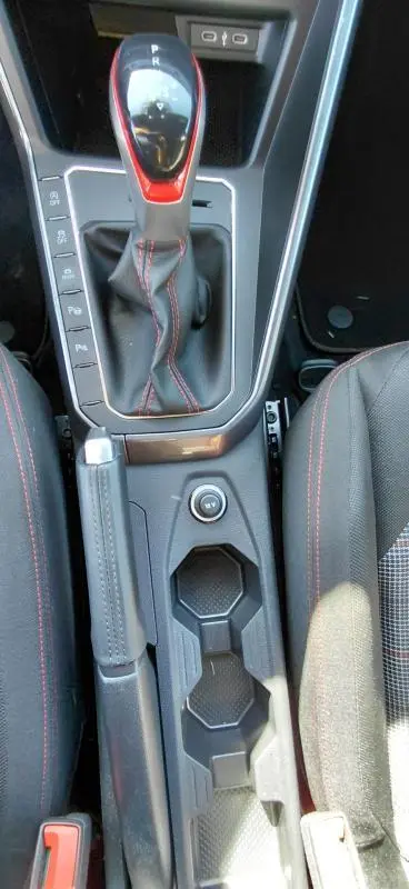 Vue rapprochée de la console centrale de la Volkswagen Polo GTI 2024 noire, avec levier de vitesse DSG7 et coutures rouges sport.