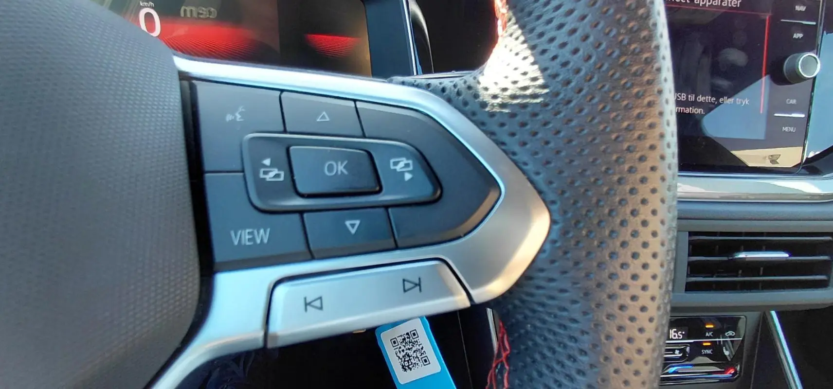 Gros plan sur le volant sport perforé de la Volkswagen Polo GTI 2024 avec commandes intégrées et cockpit numérique en arrière-plan.