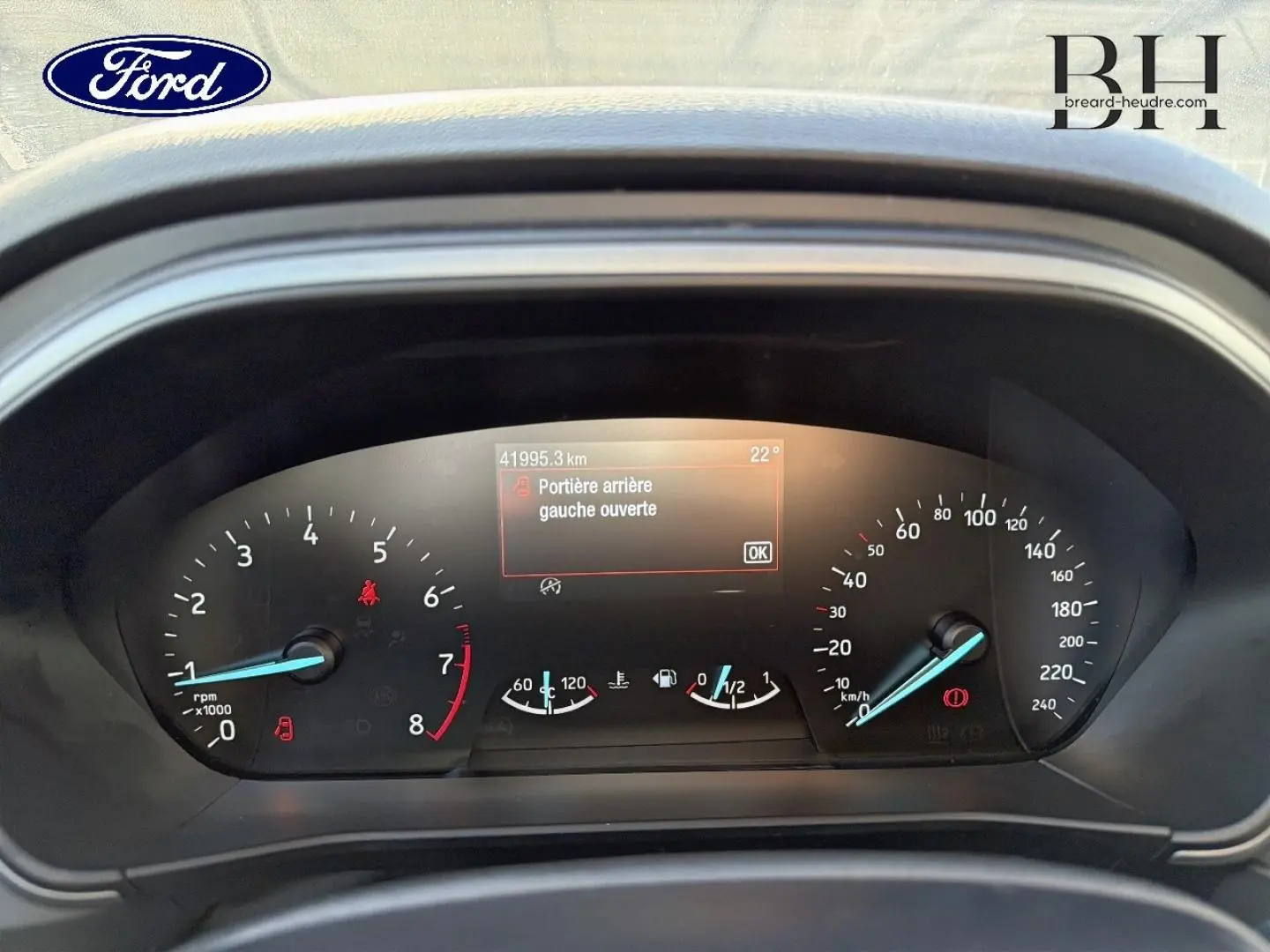 Vue rapprochée du tableau de bord de la Ford Focus bleu azur, affichant un message d'alerte porte arrière gauche ouverte.