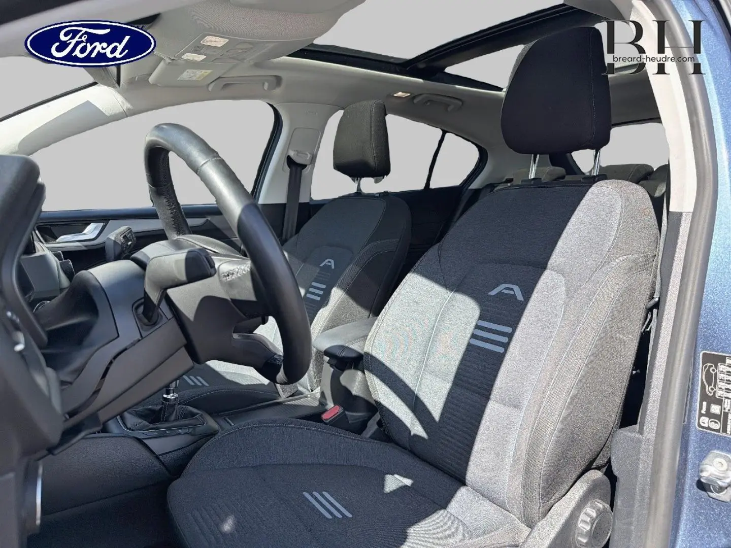 Vue intérieure côté conducteur de la Ford Focus 1.0 Flexifuel 2022, sièges tissu noir avec toit panoramique bleu azur visible.