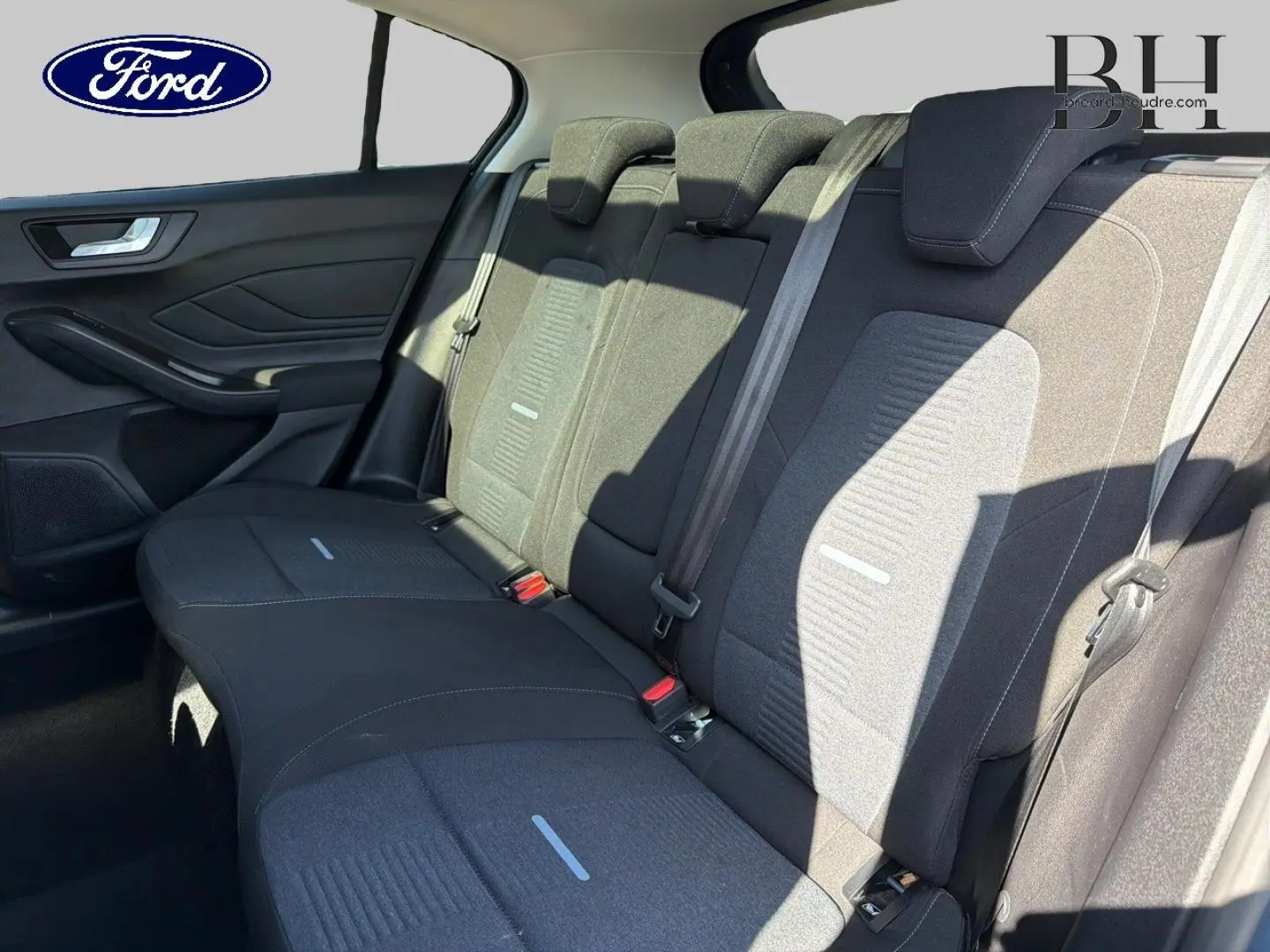 Vue latérale intérieure montrant la banquette arrière noire avec appuie-têtes et ceintures de sécurité grises d'une Ford Focus.