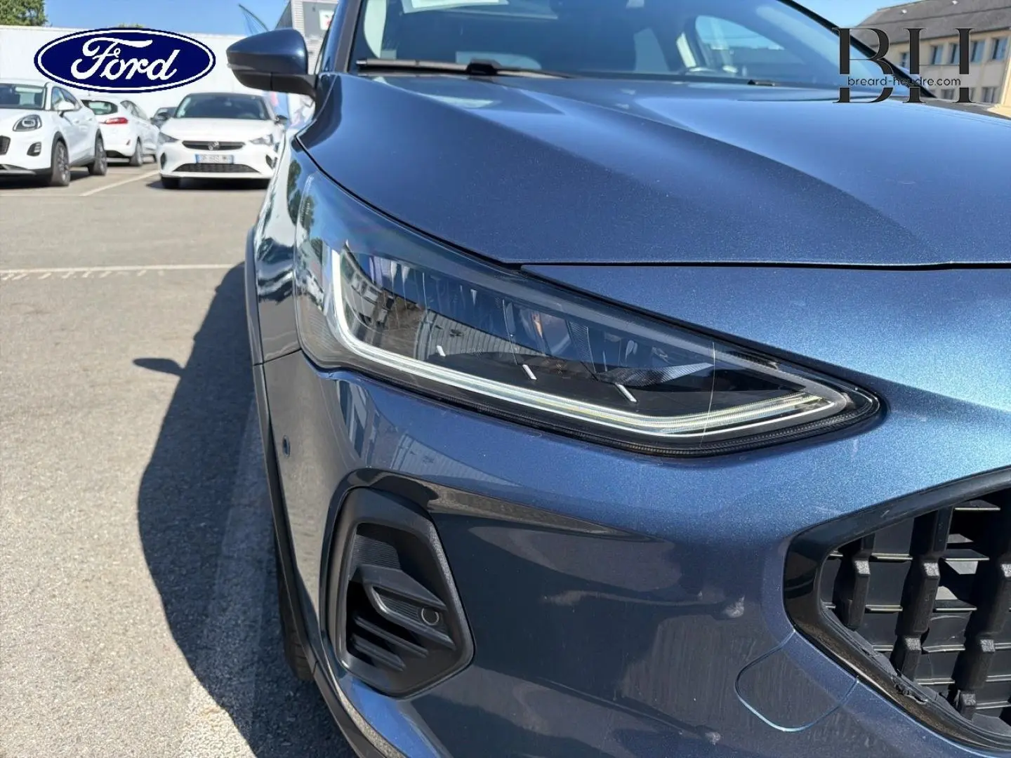 Gros plan sur l'avant gauche de la Ford Focus bleu azur métallisé, mettant en valeur le phare LED et la calandre noire.