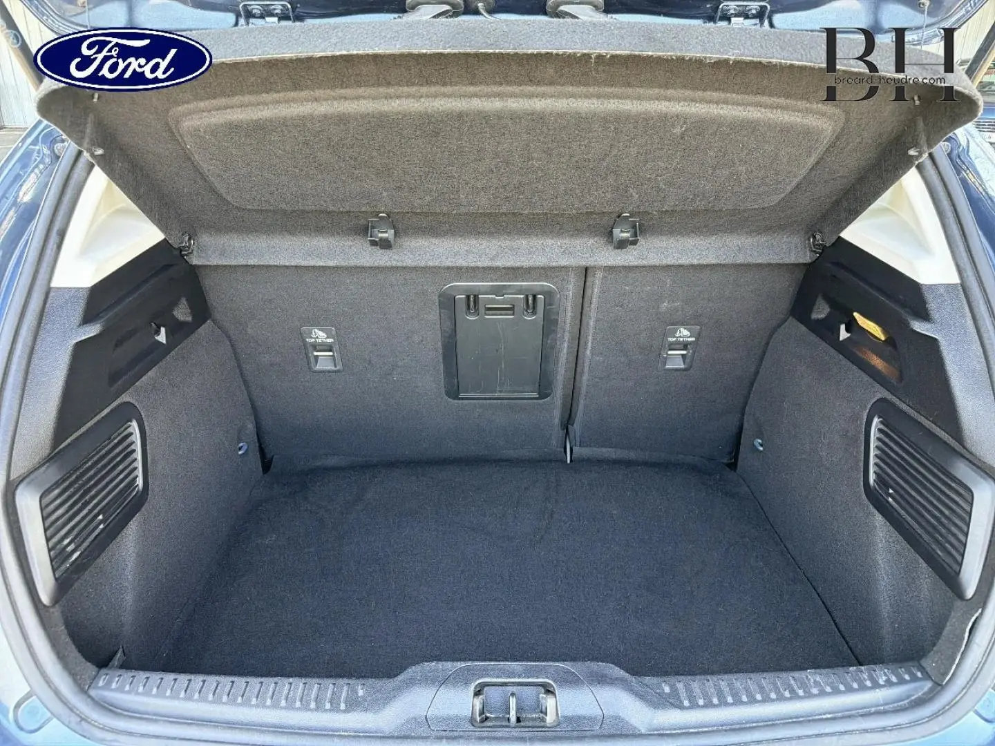 Coffre ouvert vu de l'arrière de la Ford Focus bleu azur métallisé, montrant un espace de chargement propre et bien agencé.