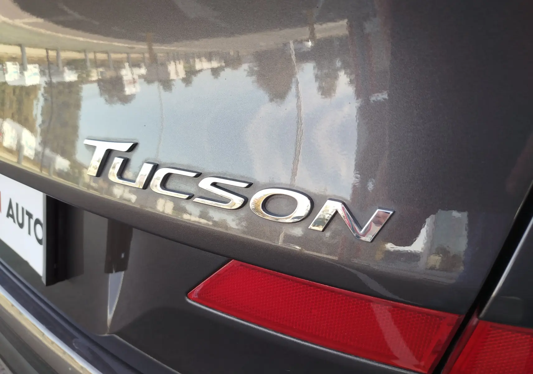 Gros plan sur le logo Tucson à l'arrière d'un Hyundai Tucson gris micron avec feu arrière rouge visible.