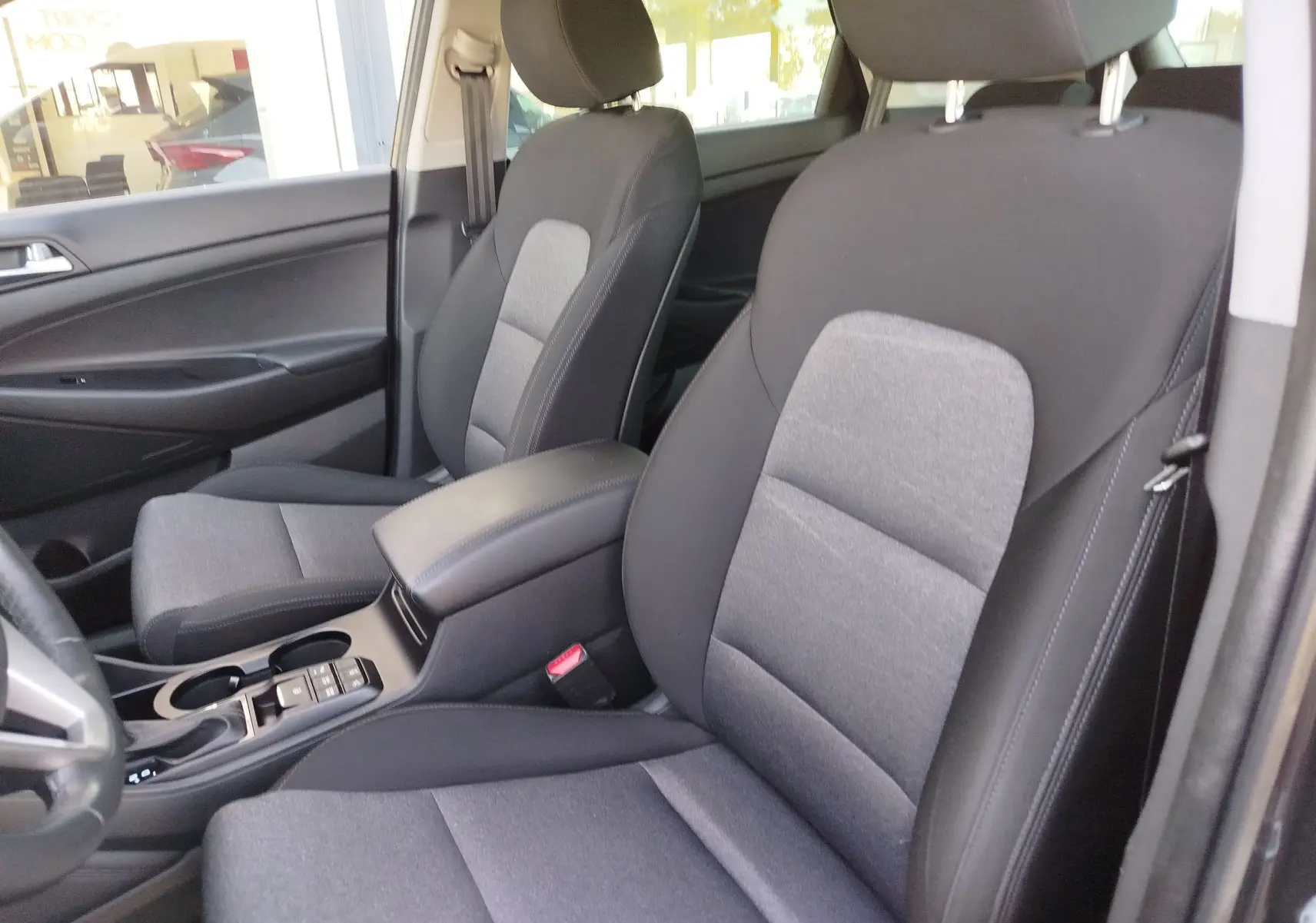 Vue intérieure côté conducteur du Hyundai Tucson 2019, sièges tissu gris foncé avec accoudoir central noir.