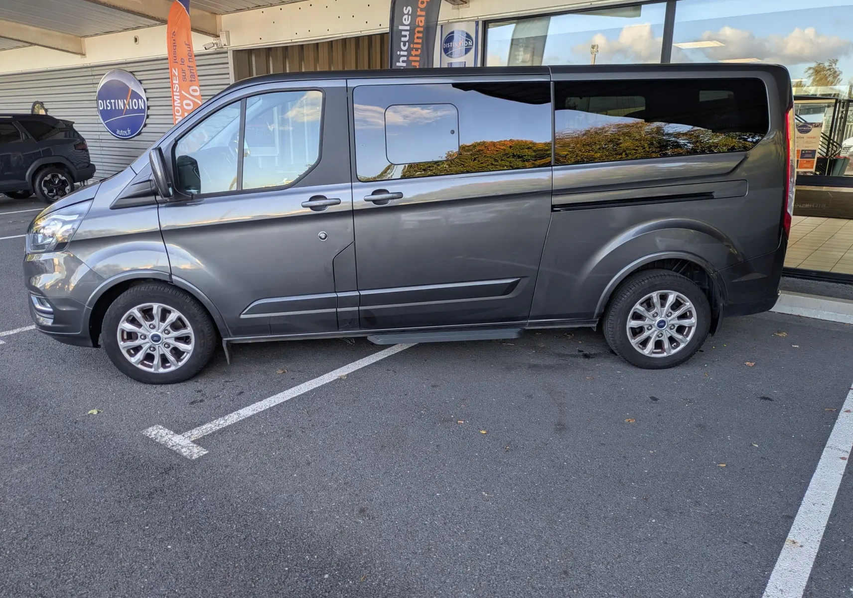 Vue de profil côté gauche d’un Ford Tourneo Custom gris 2019, grand van familial avec vitres teintées et jantes alliage.