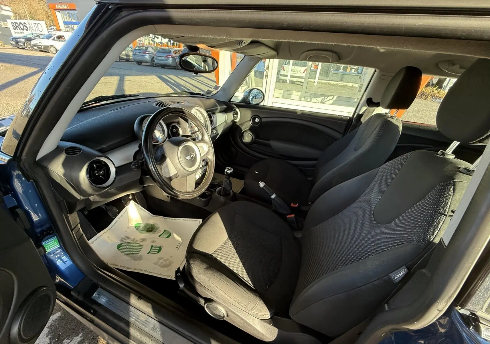 Intérieur de MINI Cooper bleu 2007 vu côté gauche, montrant sièges tissu gris et tableau de bord noir.