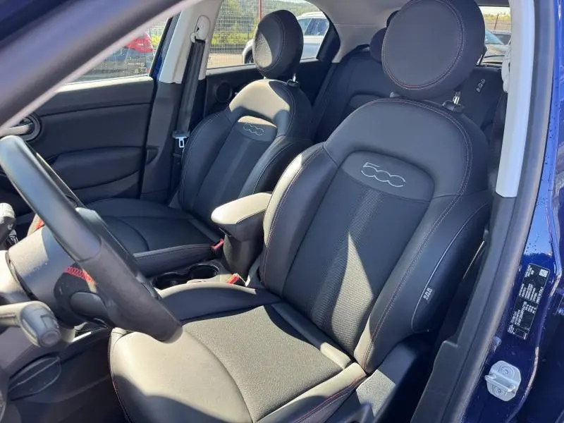Vue intérieure côté conducteur du Fiat 500X 2024 avec sièges noirs en tissu et cuir, logo 500 brodé sur les appuie-têtes.